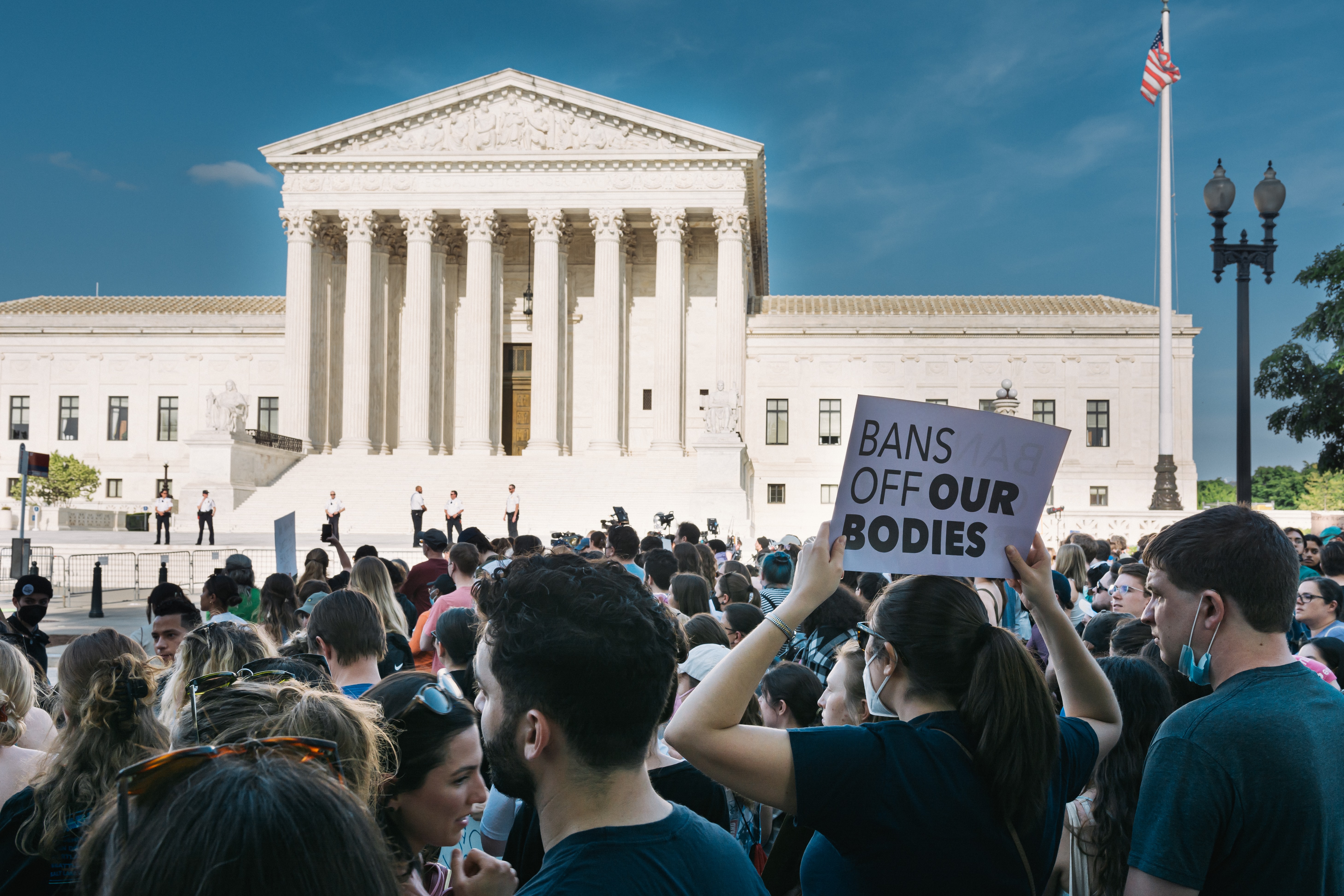 The US Supreme Court building with many protestors outside. One visible sign reads "Ban off our bodies"