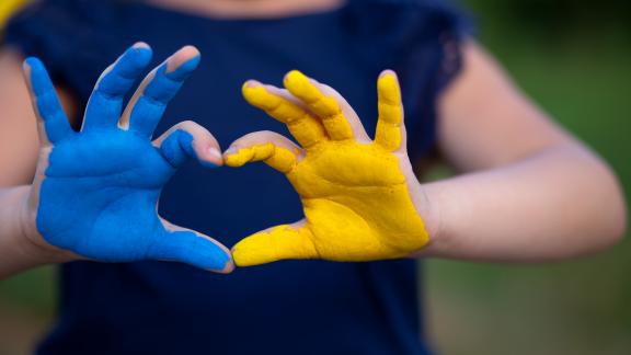 A picture of someone making a love heart with their hands. One hand is blue, the other yellow in the colours of the Ukrainian 